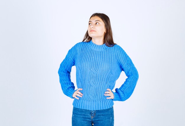 Giovane ragazza castana in maglione blu che pensa sul bianco.