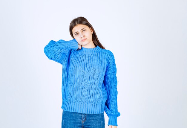 Giovane ragazza castana in maglione blu che si sente stanca su bianco.