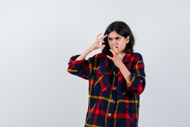 Giovane ragazza che allunga le mani in modo arrabbiato in camicia a quadri e sembra furiosa. vista frontale.