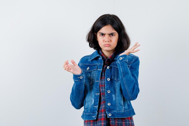 Giovane ragazza che allunga le mani in modo interrogativo in camicia a quadri e giacca di jeans e sembra sconcertata.