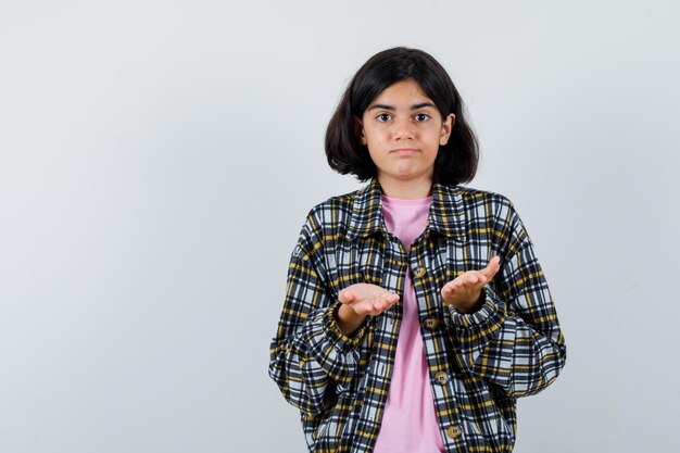 Giovane ragazza che allunga le mani mentre riceve qualcosa in camicia a quadri e t-shirt rosa e sembra carina, vista frontale.