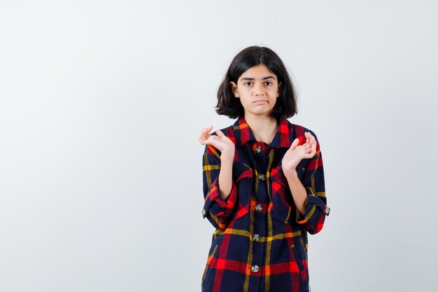 Giovane ragazza che allunga le mani mentre tiene qualcosa in camicia a quadri e sembra carina, vista frontale.