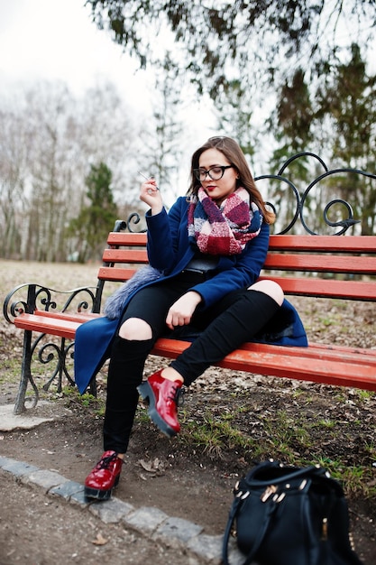 Giovane ragazza che fuma sigaretta all'aperto seduta su una panchina Concetto di dipendenza da nicotina da parte degli adolescenti