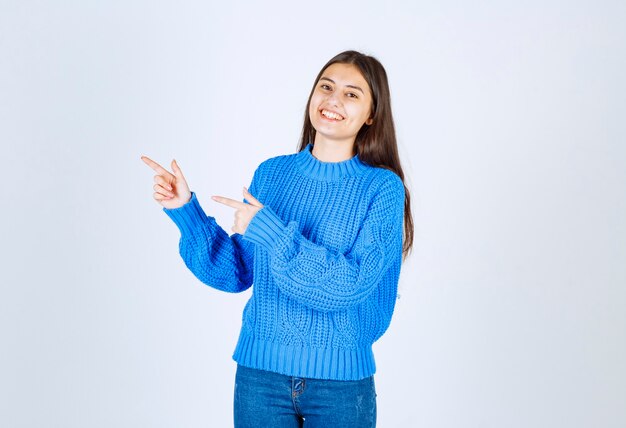 giovane ragazza che indica al suo fianco mentre sorride su bianco.