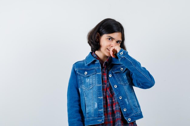 Giovane ragazza che mette la mano sulla bocca, sorride in camicia a quadri e giacca di jeans e sembra felice. vista frontale.