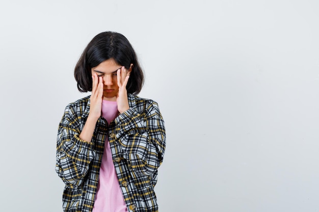 Giovane ragazza che mette le mani sul viso, si sfrega le tempie mentre chiude gli occhi in camicia a quadri e maglietta rosa e sembra stanca