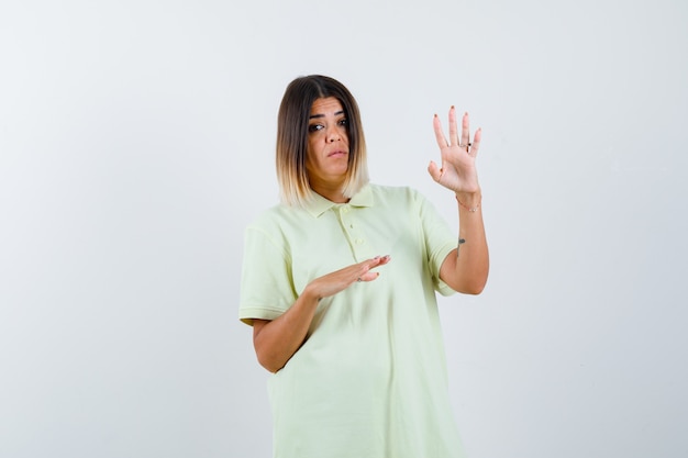 Giovane ragazza che mostra il segnale di stop, allungando una mano da parte in maglietta e guardando concentrato, vista frontale.