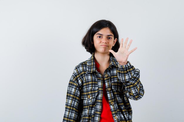 Giovane ragazza che mostra il segnale di stop in camicia a quadri e maglietta rossa e sembra allegra, vista frontale.