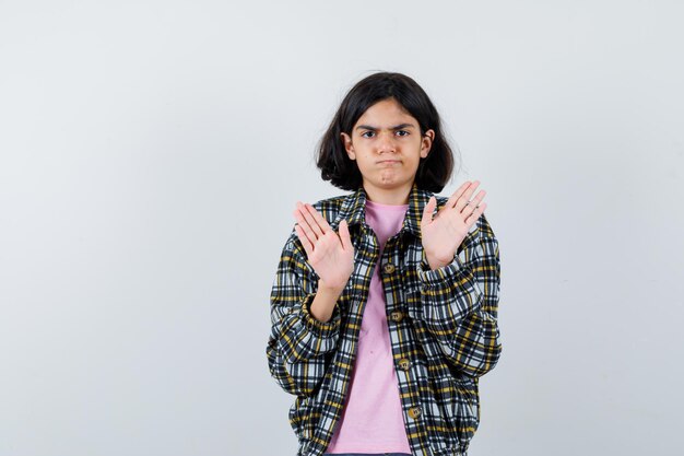 Giovane ragazza che mostra segnali di stop in camicia a quadri e t-shirt rosa e sembra seria. vista frontale.