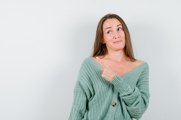 Giovane ragazza che punta a sinistra con il dito indice, guardando lontano in maglieria e guardando felice, vista frontale.