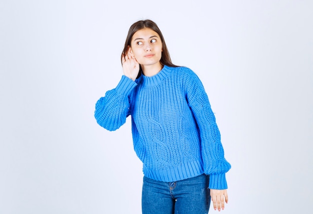 giovane ragazza che punta cercando di ascoltare qualcosa su bianco.