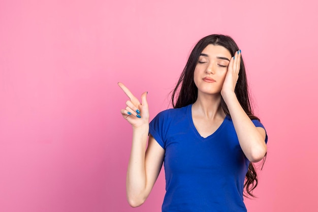 Giovane ragazza che tiene la mano sulla testa e punta il dito da parte Foto di alta qualità