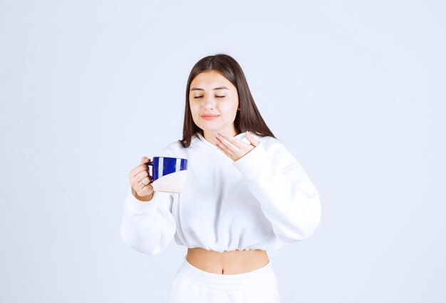 giovane ragazza che tiene una tazza su sfondo bianco-grigio.