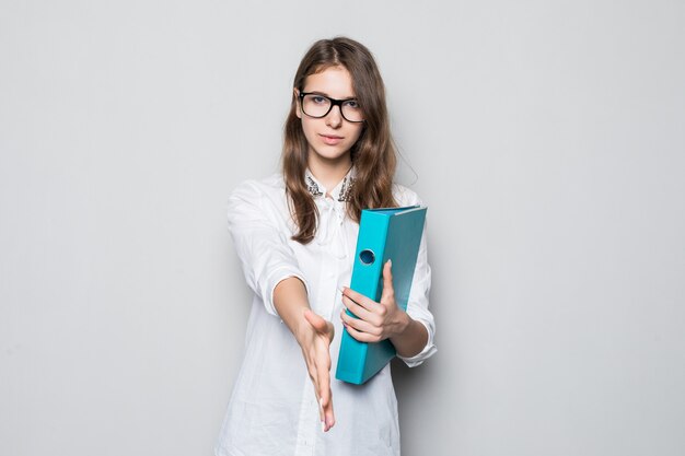 Giovane ragazza con gli occhiali vestita in t-shirt bianca da ufficio rigoroso si trova di fronte al muro bianco con la cartella blu per i documenti nelle sue mani
