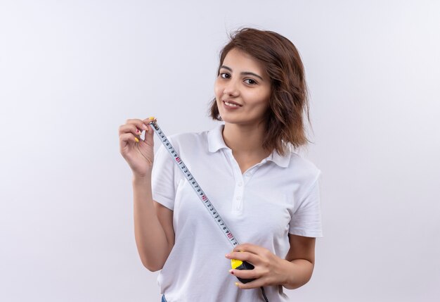 Giovane ragazza con i capelli corti che indossa la polo bianca utilizzando la misura addomesticare sorridente con la faccia felice