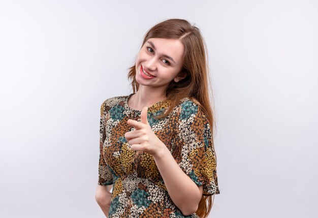 Giovane ragazza con i capelli lunghi che indossa abiti colorati positivo e felice che punta con il dito indice alla fotocamera