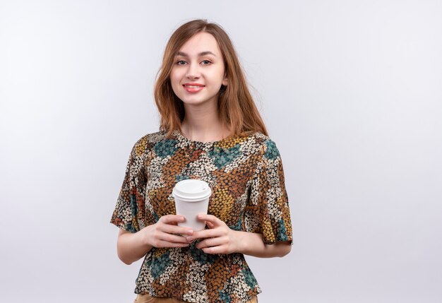 Giovane ragazza con i capelli lunghi che indossa abiti colorati tenendo la tazza di caffè sorridente fiducioso