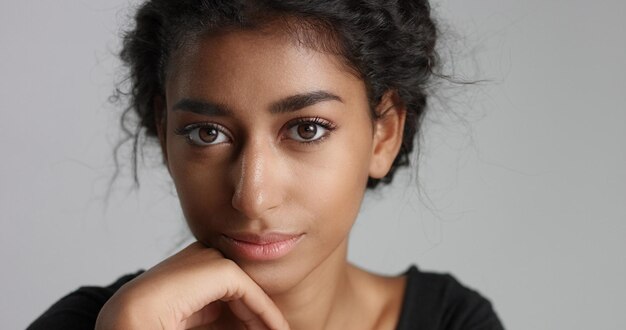 Giovane ragazza con perfetta pelle marrone chiaro e bei capelli neri ricci che sorride alla macchina fotografica in studio