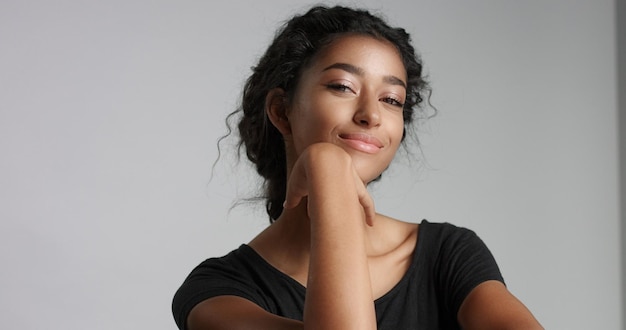 Giovane ragazza con perfetta pelle marrone chiaro e bei capelli neri ricci che sorride alla macchina fotografica in studio