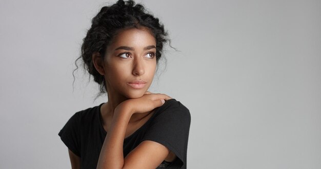 Giovane ragazza con perfetta pelle marrone chiaro e bei capelli neri ricci che sorride alla macchina fotografica in studio