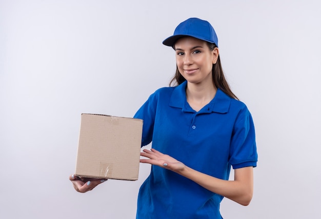 Giovane ragazza di consegna in uniforme blu e pacchetto della scatola della tenuta del cappuccio che sorride sicuro