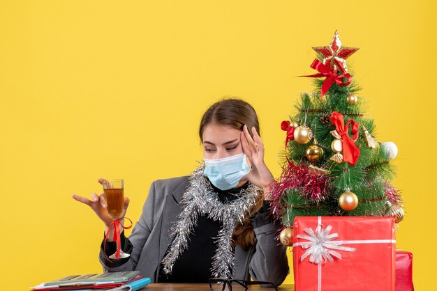 Giovane ragazza di vista frontale con mascherina medica che si siede al tavolo che indica con il dito