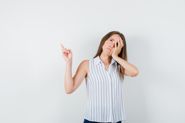 Giovane ragazza faccia pendente sul palmo con il dito in t-shirt, jeans e guardando stanco, vista frontale.