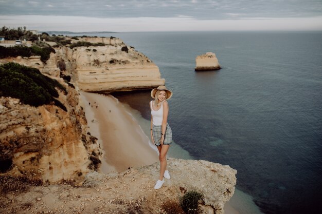 Giovane ragazza felice sul bordo della pietra con vista panoramica sulla spiaggia del mare.