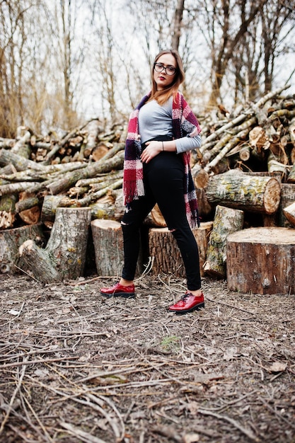 Giovane ragazza hipster indossare su coperta e occhiali contro ceppi di legno su legno