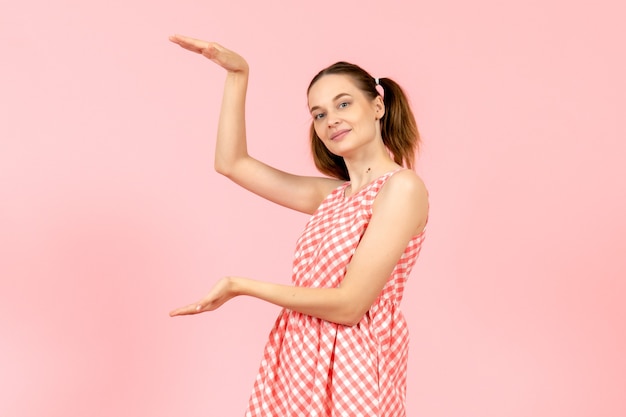 giovane ragazza in abito rosa carino che mostra le dimensioni sul rosa