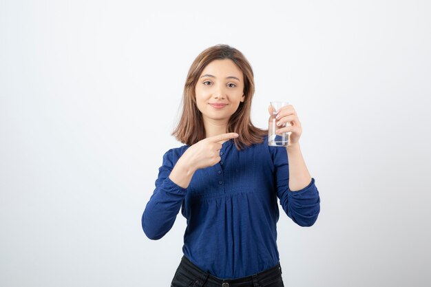 Giovane ragazza in blu che punta all'acqua in mano sul muro bianco.