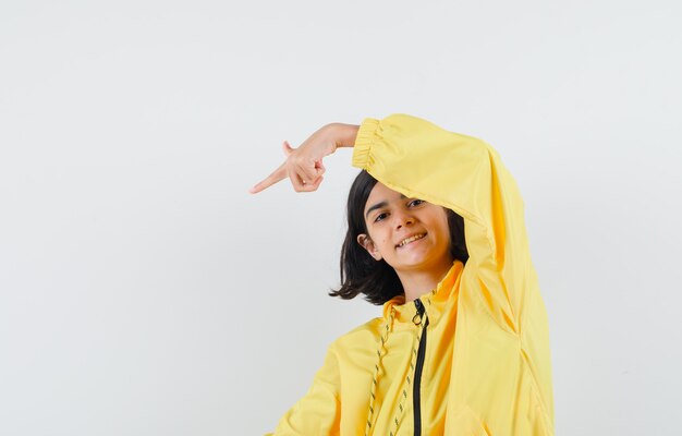 Giovane ragazza in bomber giallo e gonna rosa che punta nell'angolo inferiore sinistro con il dito indice e sembra felice