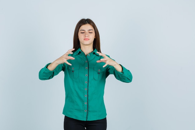 Giovane ragazza in camicetta verde, pantaloni neri che allungano le mani come tenendo qualcosa di immaginario e guardando concentrato, vista frontale.