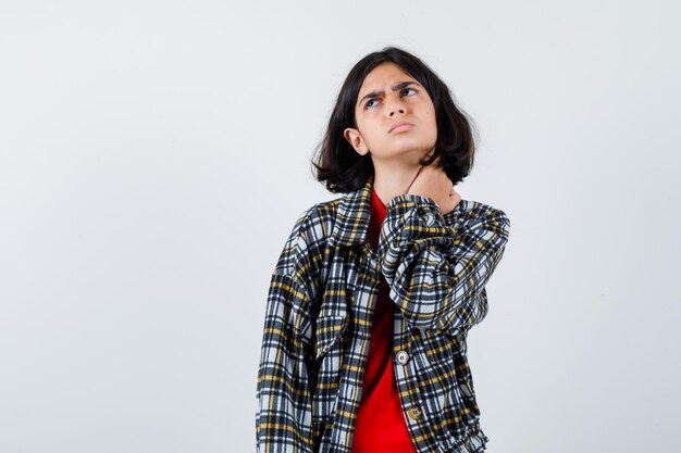 Giovane ragazza in camicia a quadri e t-shirt rossa che mette la mano sul collo, guarda sopra e sembra tormentata, vista frontale.