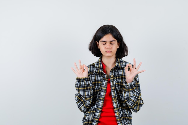 Giovane ragazza in camicia a quadri e t-shirt rossa in piedi in posa meditativa e sembra calma, vista frontale.