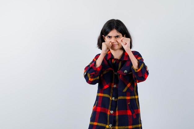 Giovane ragazza in camicia a quadri in piedi nella posa del pugile e guardando furiosa, vista frontale.