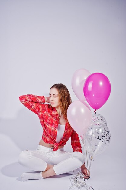 Giovane ragazza in camicia a quadri rossa e pantaloni bianchi con palloncini su sfondo bianco in studio