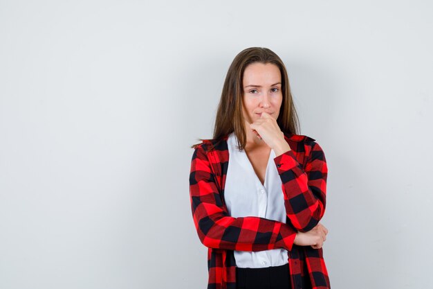 Giovane ragazza in camicia a scacchi, camicetta con la mano sulla bocca e dall'aspetto sensato, vista frontale.