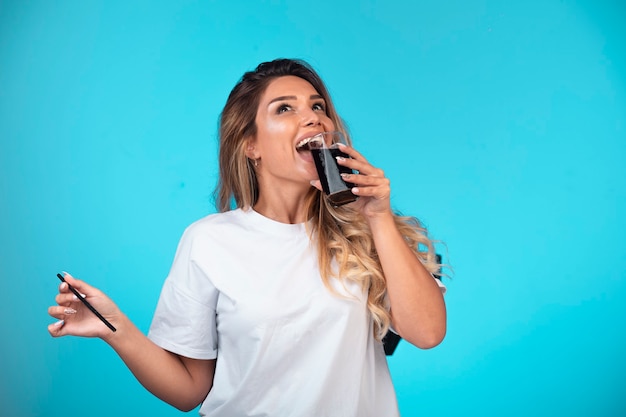 Giovane ragazza in camicia bianca, bere un bicchiere di cocktail nero.