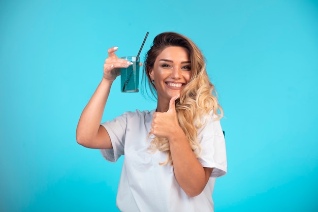 Giovane ragazza in camicia bianca con in mano un bicchiere di cocktail blu.