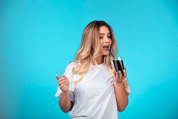 Giovane ragazza in camicia bianca con in mano un bicchiere di cocktail nero e berlo.