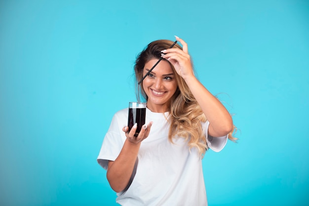 Giovane ragazza in camicia bianca con in mano un bicchiere di cocktail nero e controllando il gusto.