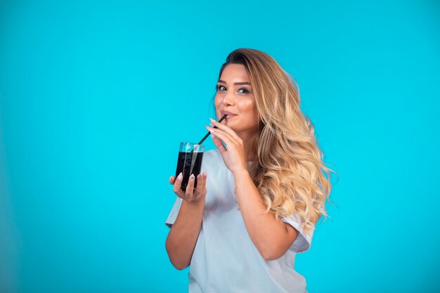 Giovane ragazza in camicia bianca con in mano un bicchiere di cocktail nero e controllando il gusto