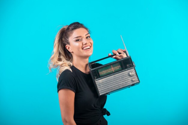 Giovane ragazza in camicia nera che tiene una radio vintage e si sente positiva.