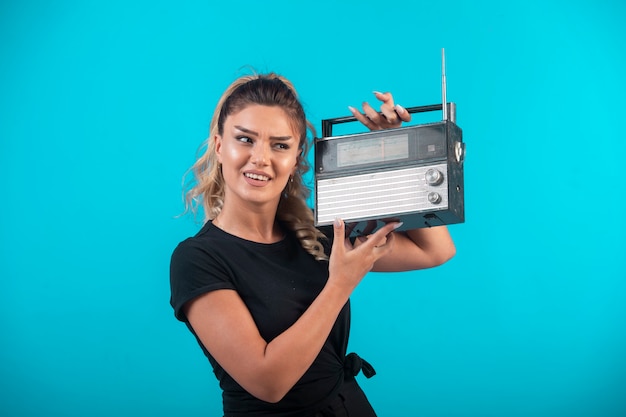 Giovane ragazza in camicia nera che tiene una radio vintage sulla spalla e si sente positiva.