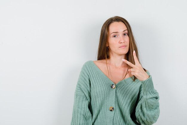 Giovane ragazza in maglieria che mostra gesto di pace e guardando fiducioso, vista frontale.