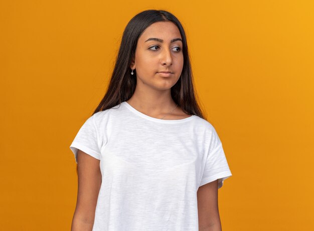 Giovane ragazza in maglietta bianca che guarda da parte con un'espressione seria e sicura in piedi sopra l'arancia