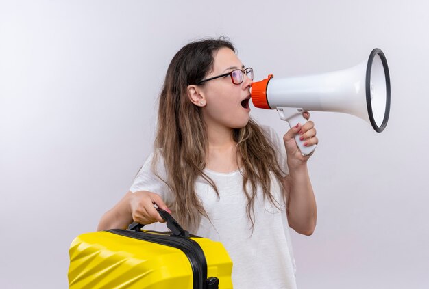 Giovane ragazza in maglietta bianca che tiene la valigia di viaggio che grida al megafono