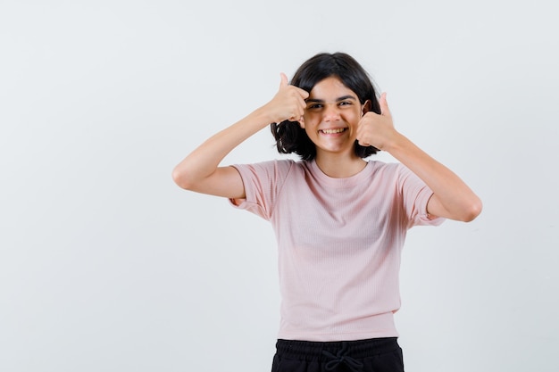 Giovane ragazza in maglietta rosa e pantaloni neri che mostra i pollici in su con entrambe le mani e sembra felice