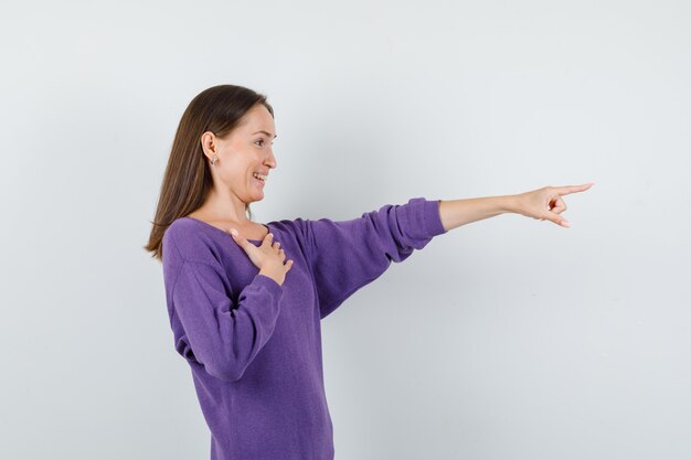 Giovane ragazza in maglietta viola che punta al lato e che sembra felice, vista frontale.